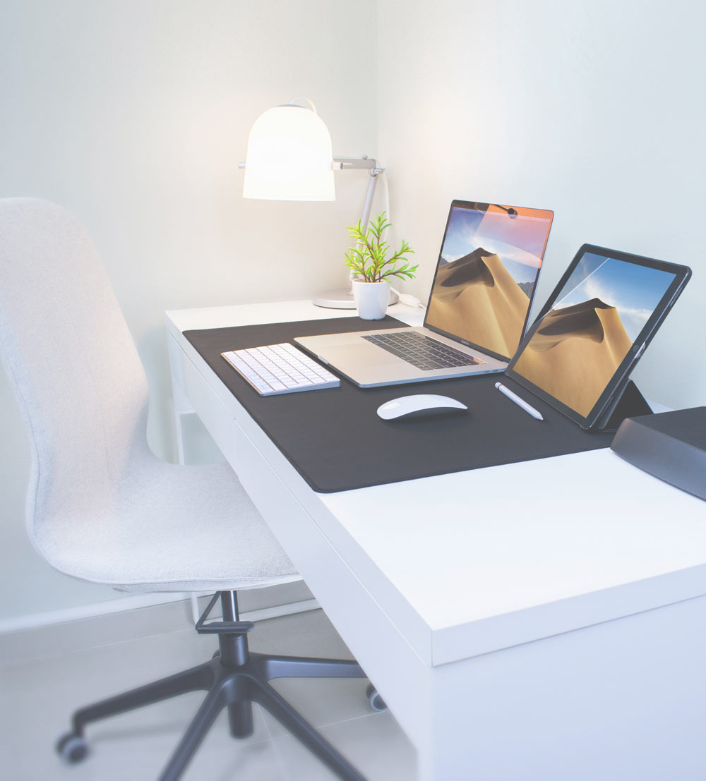 A laptop and iPad tablet on a white desk with a white chair pushed underneath