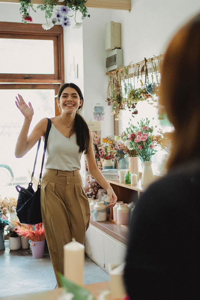 A customer walking into a shop smiling and waving at the employee