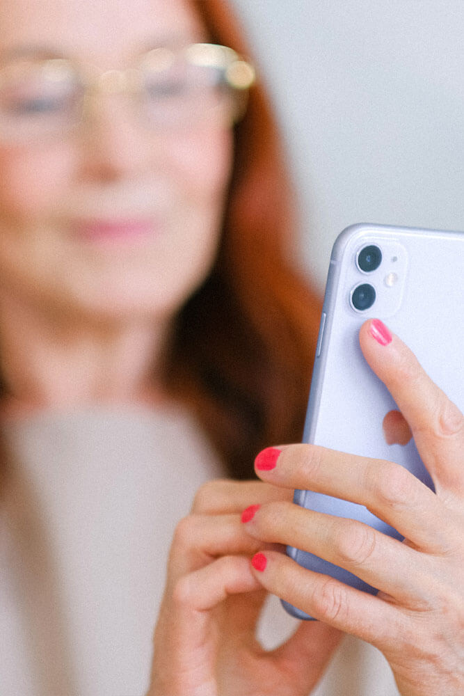 A close up photo of a person with red hair holds a phone up and is looking at it. The person is out of focus and the phone is in focus.